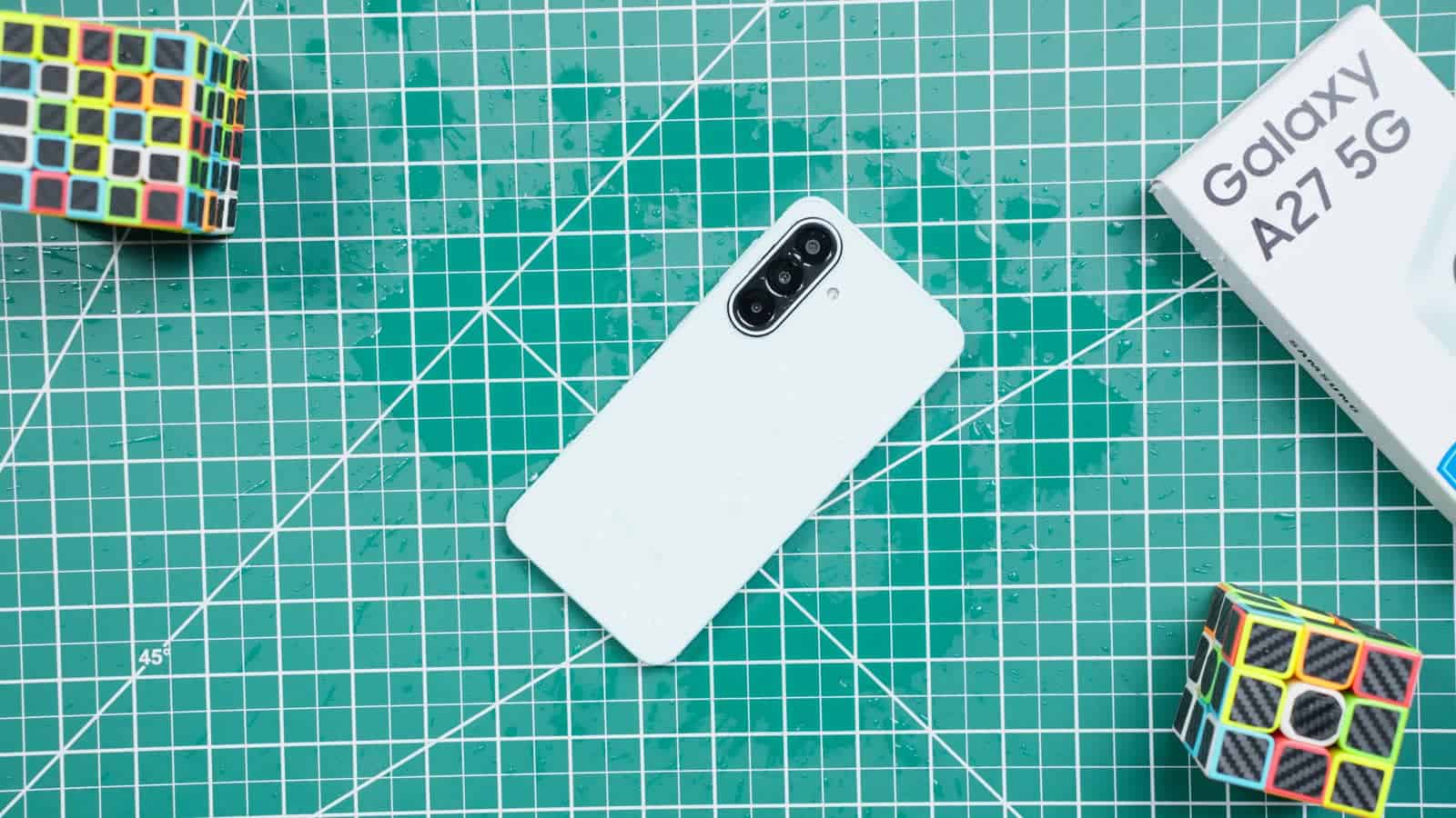 The Galaxy A27 5G lying on a cutting mat with drops of water on its back