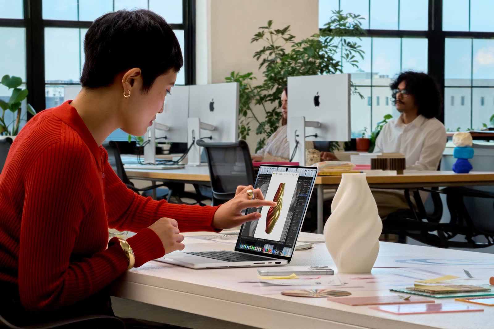 A person at a desk touching the screen of the MacBook Pro with PROLED XDR Display while a 3D object is open
